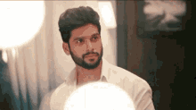 a man with a beard and a white shirt is looking at himself in the mirror .