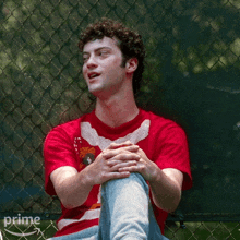 a man wearing a red shirt is sitting on a fence with the word prime on the bottom