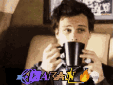 a man is drinking from a black mug with the word batan in the corner