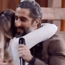 a man with a beard is hugging a woman with a microphone in his hand .