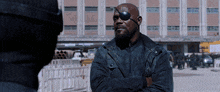 a man wearing a black jacket and a black eye patch stands with his arms crossed