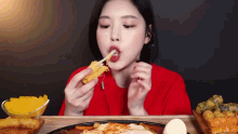 a woman in a red shirt is eating a sandwich with a toothpick in her mouth .