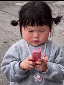 a little girl wearing a sweater that says ato is holding a pink toy phone