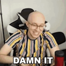a bald man wearing glasses is sitting in a chair with the words `` damn it '' written on his face .