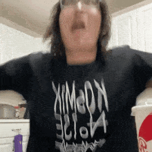 a woman wearing a black t-shirt with the word hope on it is standing in a kitchen .