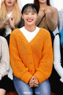 a woman wearing an orange sweater is smiling in front of a group of women