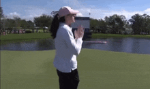 a woman is standing on a golf course wearing a pink hat and clapping .