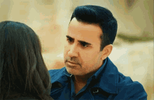 a man in a blue jacket looks at a woman in a black shirt