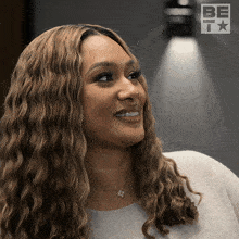 a woman with wavy hair is smiling in front of a sign that says be