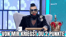 a man with a beard and red lips is sitting in a chair with a crown on it .
