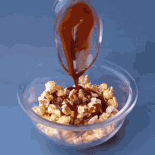 a person is mixing popcorn with chocolate sauce in a glass bowl
