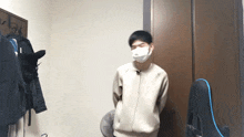 a young man wearing a mask is standing in a room next to a chair .