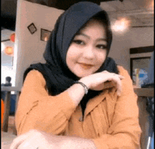 a woman wearing a hijab and a yellow shirt is sitting at a table in a restaurant .