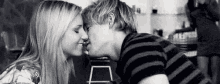 a black and white photo of a man and woman kissing in a restaurant .
