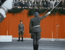 a man in a military uniform stands in front of a crowd holding a flag
