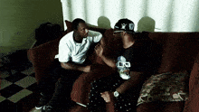 two men sitting on a couch with one wearing a shirt that says ' a bathing ape ' on it