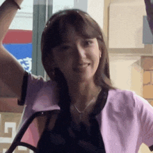 a woman wearing a pink jacket and a black top is smiling with her arm in the air