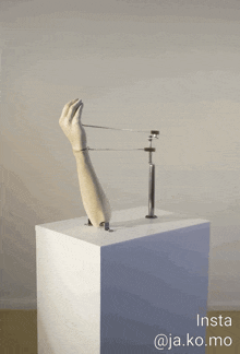 a statue of a hand on a white pedestal with insta @ja.ko.mo written below it