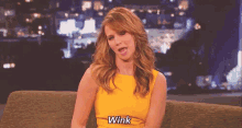 a woman in a yellow dress says wink while sitting on a couch .