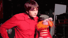 a pixelated image of a man in a red shirt holding a muppet