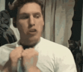 a man in a white shirt is adjusting his tie in a room .