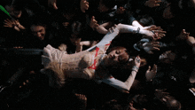 a woman in a white top is surrounded by a crowd of people with their hands outstretched