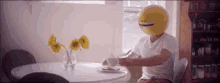 a man with a smiley face on his head is sitting at a table drinking coffee