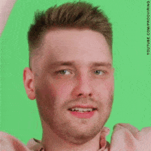 a man with a beard and a pink shirt is smiling and looking at the camera .