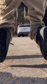 a person is standing on a sidewalk with their feet up and a car in the background .
