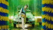 a man is standing next to a car in a car wash holding a hose .
