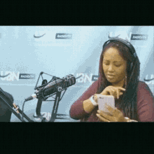 a woman wearing headphones looks at her phone in front of a radio station