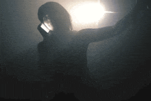 a woman is standing in a dark room with a light shining on her