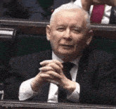 a man in a suit and tie is sitting in a parliament with his hands folded .
