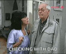 a man and a woman are standing next to each other in a living room and the woman is talking to the man .