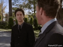 two men in suits and ties are standing next to each other looking at each other .