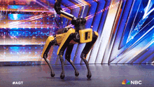 a yellow and black robot is dancing on a stage with a nbc logo in the corner
