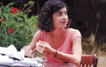 a woman in a pink polka dot shirt is sitting at a table with a fork in her hand