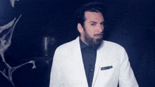 a man with a beard is wearing a white jacket and black shirt