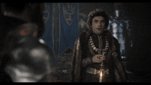 a man with a crown on his head is talking to another man in a foreign language
