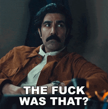 a man with a mustache is sitting in front of a sign that says the fuck was that