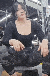 a woman is sitting on a bench in a gym wearing leggings and a black top .