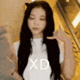 a woman with long black hair is wearing a white shirt and giving a thumbs up sign .