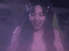a close up of a woman in a pink dress smiling in a dark room .