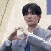 a young man in a suit and tie is making a heart with his hands .
