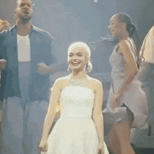 a woman in a white dress is dancing on a stage with a man and two women .