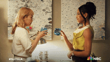 two women standing next to each other with a nbc logo on the bottom right