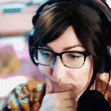 a woman wearing glasses and headphones holds her hand to her chin