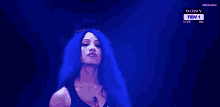 a woman with long blue hair is standing in front of a blue background on a television screen .