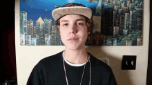 a young man wearing a hat and a necklace stands in front of a cityscape painting