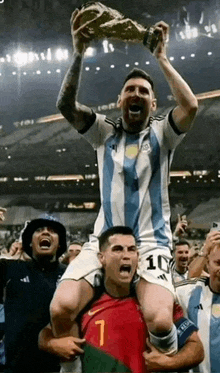 a soccer player is carrying another soccer player on his shoulders while holding a trophy on a soccer field .